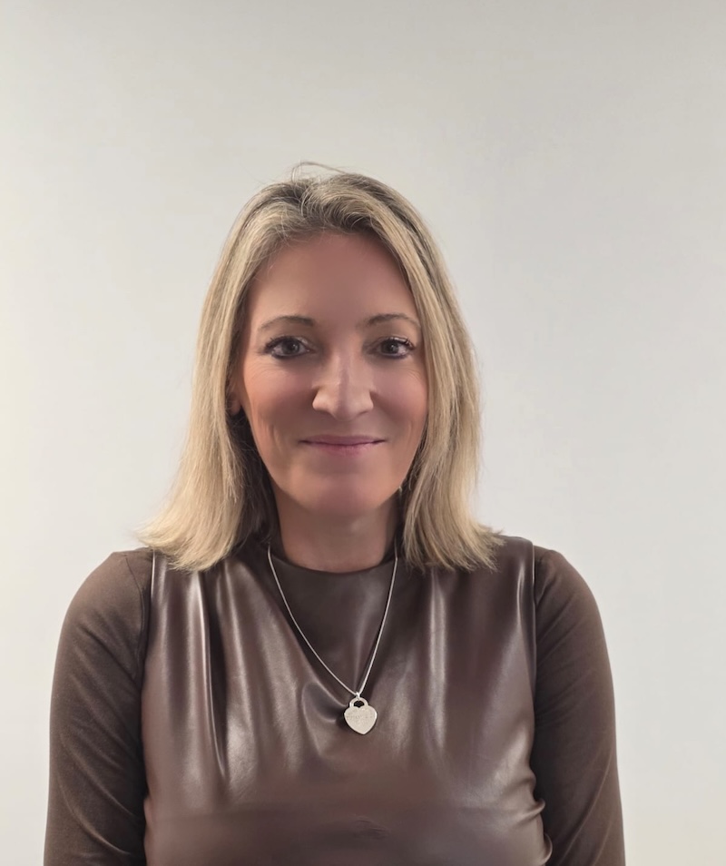 woman with blonde hair smiling with a brown top on and a heart necklace having a headshot taken for the Rowan Park team page
