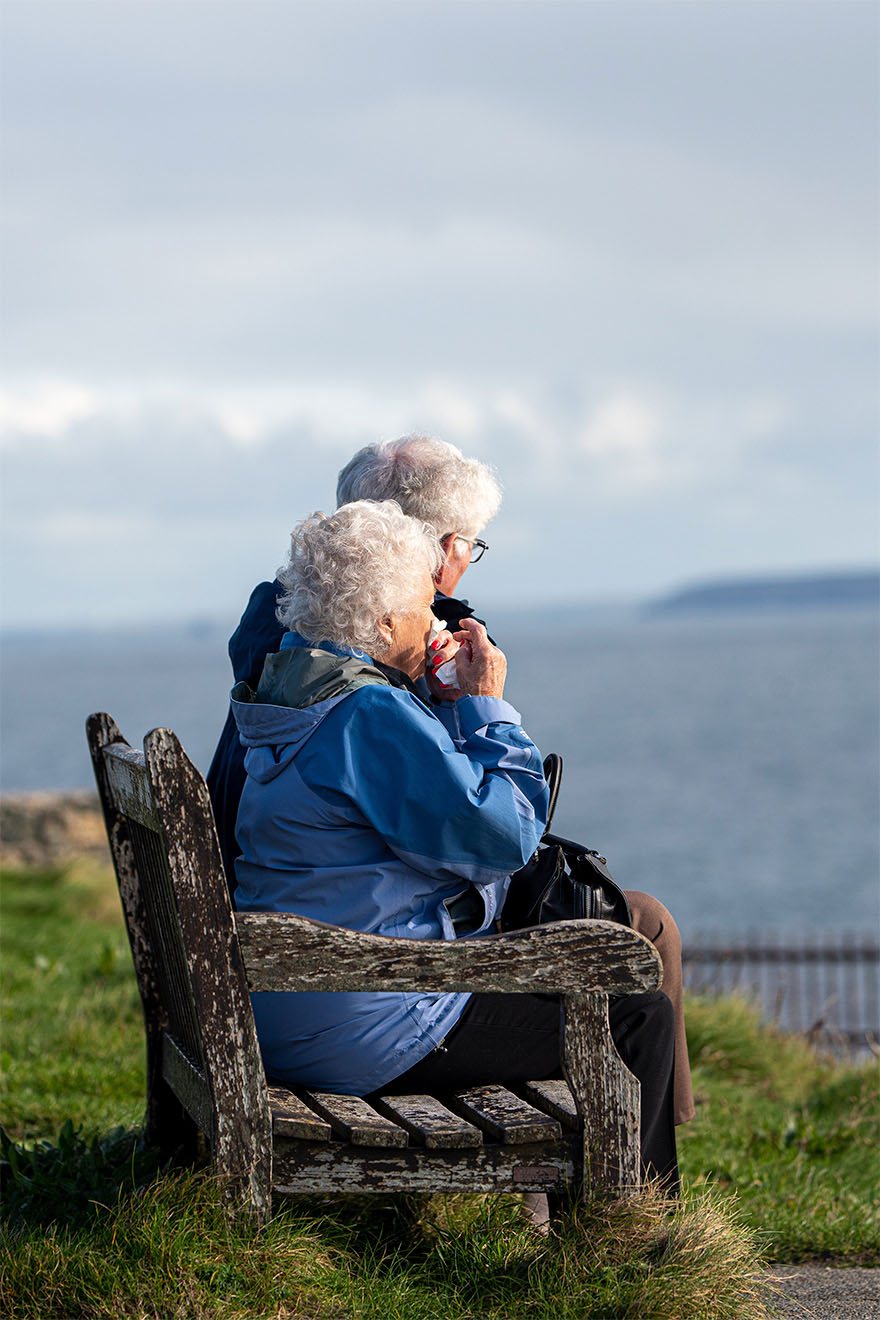 resident couple sat on bench at beach looking at the sea