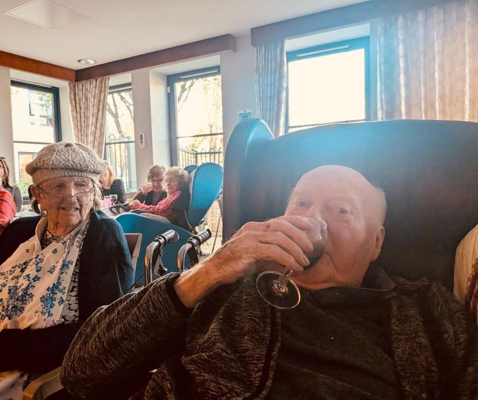 older man sat in chair having a drink with other residents