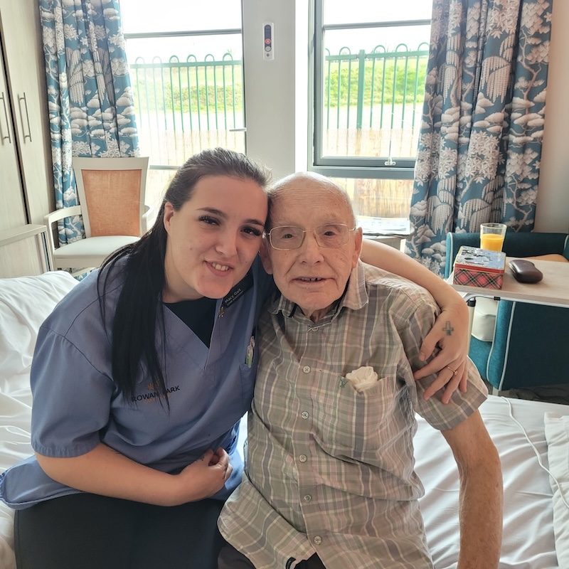 male resident sat with a carer in his room smiling