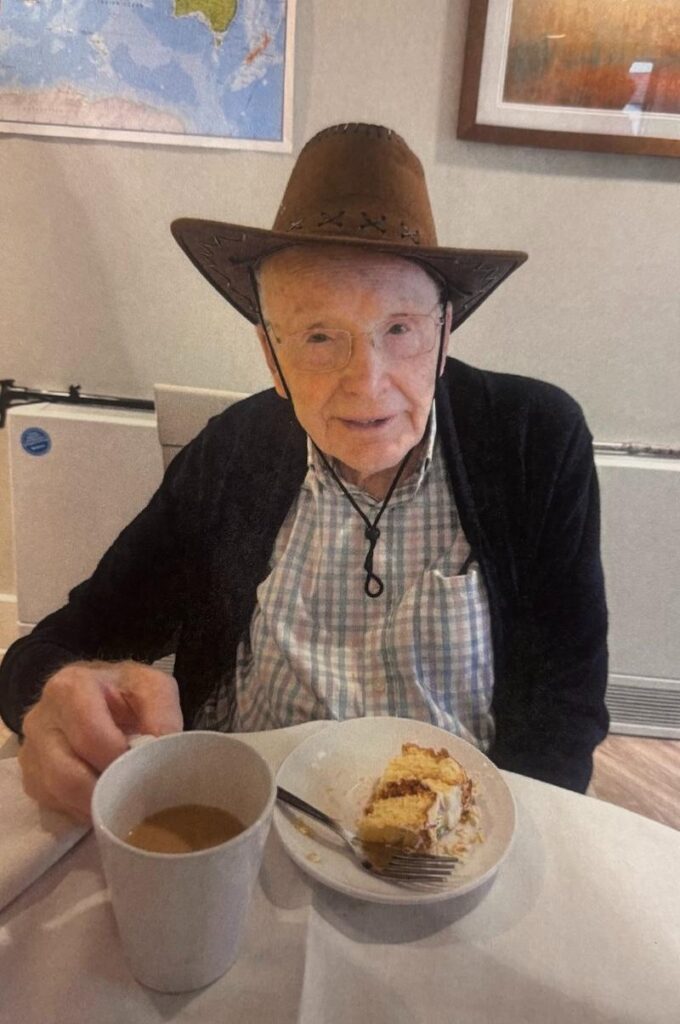 male resident wearing a hat smiling with a hot drink and slice of cake
