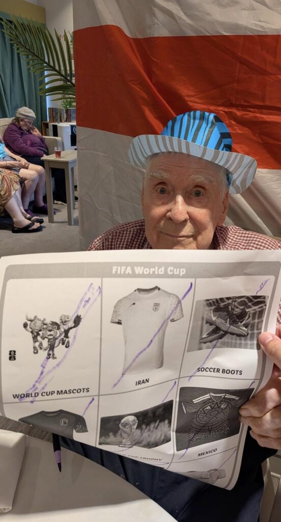 older man with a blue hat holding up fifa world cup paper