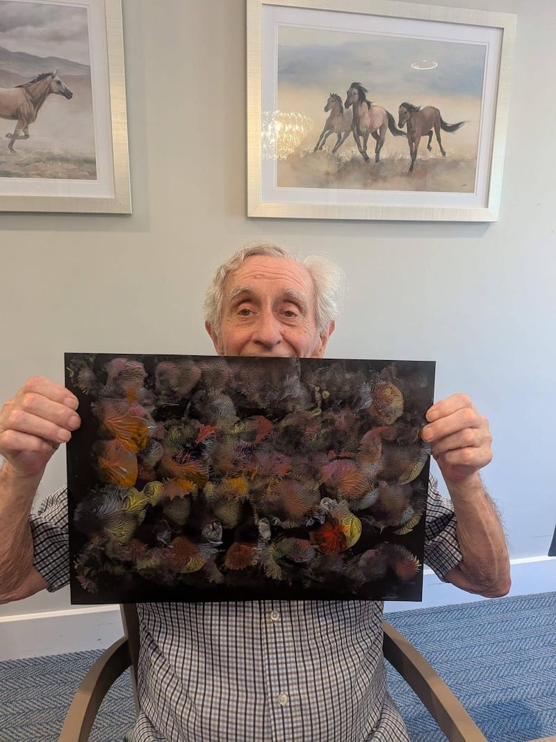 elderly man holding up a piece of abstract art he made using paint on black paper
