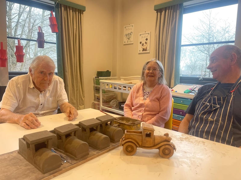 2 elderly residents sat at the table with clay trains sat in front of them
