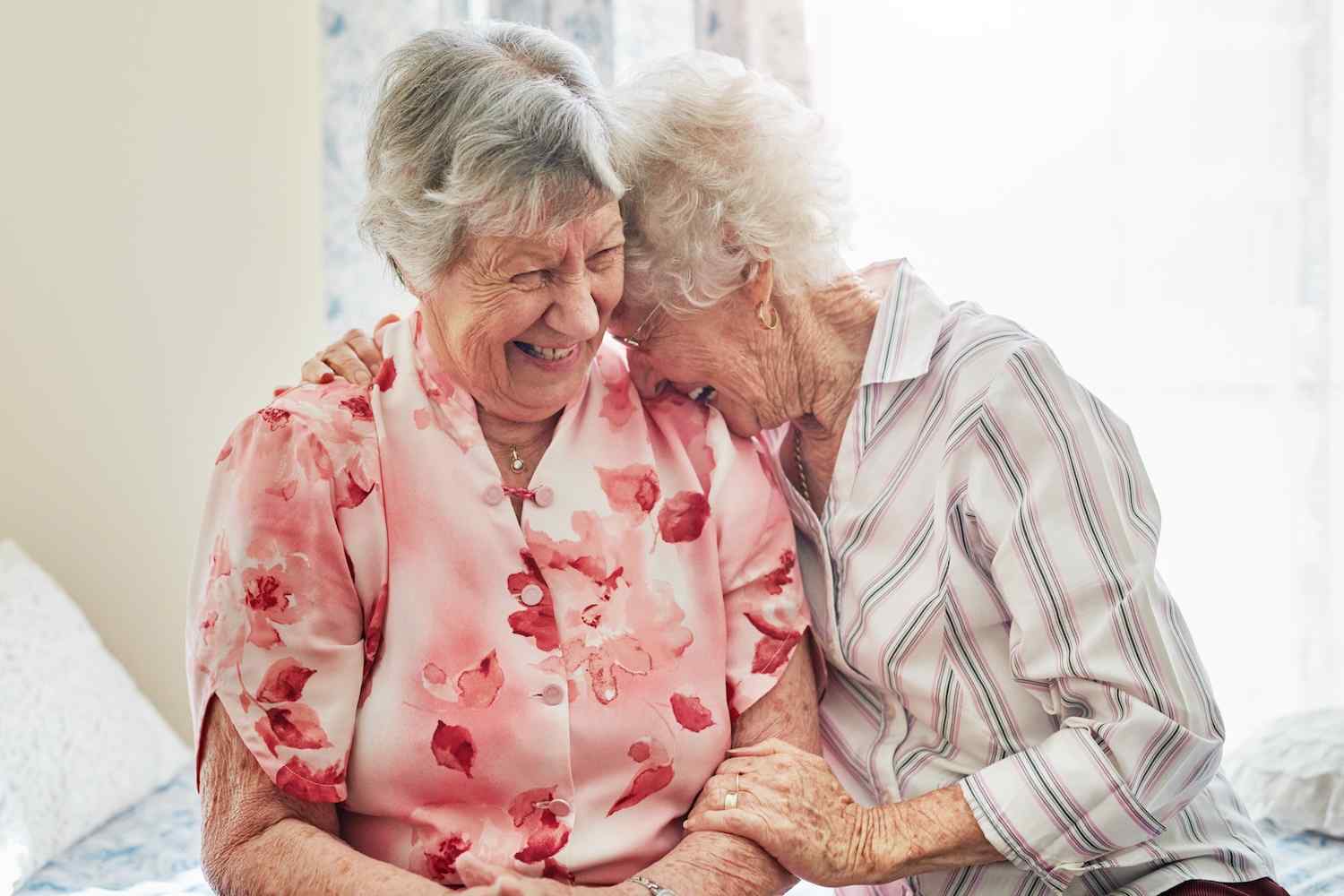 2 female residents sat on a bed together laughing