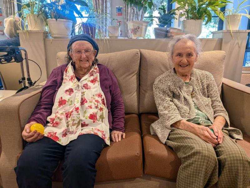 two older ladies sat on a sofa smiling